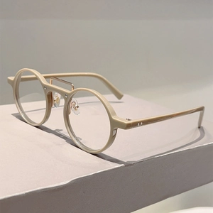 Détail de montures rondes beige avec un double pont distinctif en métal doré élégant