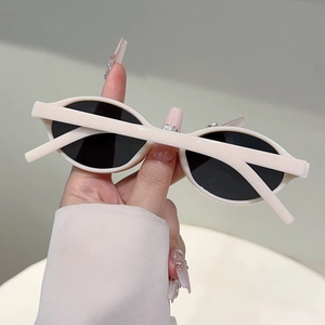 Gros plan d'une main tenant des lunettes de soleil ovales rétro beige crème et verres noirs
