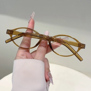 Détail des lunettes de soleil ovales ambrées translucides tenues à la main sur fond uni