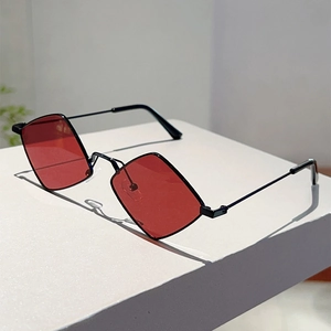 Close-up of red diamond lenses and slim black metal frame sunglasses on white surface