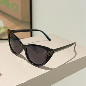 Close-up of retro black cat-eye sunglasses with dark lenses on a beige pedestal stand