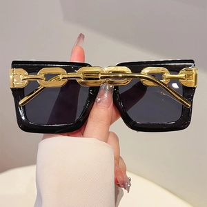 Close-up of square black sunglasses with decorative thick gold metal chain accents