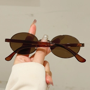 Close-up of translucent amber oval sunglasses with brown lenses held in hand