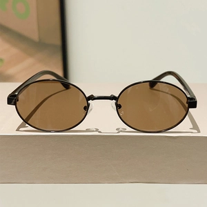 Detail view of oval metal sunglasses with brown lenses on a beige display stand