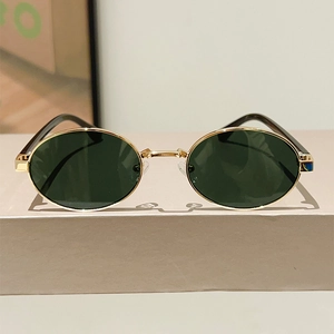 Detailed view of oval metal sunglasses with gold frames and dark green lenses on a stand