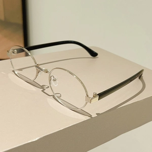Detail shot of silver oval metal frame glasses with black temples on a beige stand