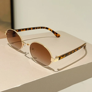Detailed close-up of oval gold metal sunglasses with brown gradient lenses and tortoise temples