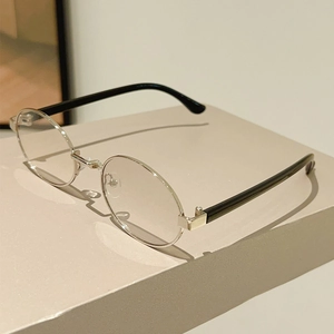 Detail view of oval silver metal frame sunglasses with black temples on a beige display stand