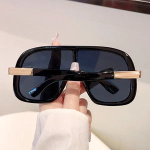 Detailed close-up of oversized black sunglasses with golden metal hinge decorations