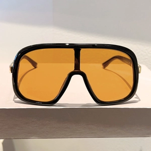 Detail view of large-frame sunglasses with shiny black frame and bright orange lens