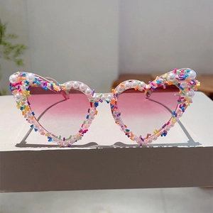 Detail einer herzförmigen Sonnenbrille mit rosa Verlaufsgläsern und Perlen-Pailletten-Besatz