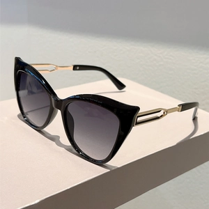 Detail of black cat-eye sunglasses with golden hollow temples on a beige stand