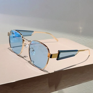Detail der ovalen Metall-Sonnenbrille in Gold mit blauen Gläsern und geometrischen Bügeln