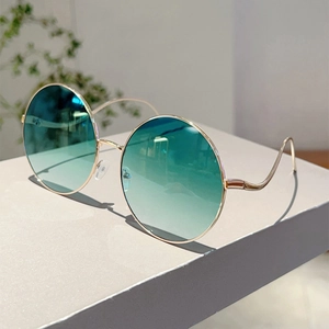 Detail of round metal sunglasses with green gradient lenses and wavy gold temples