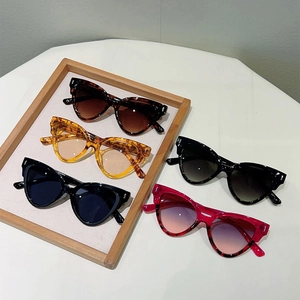 Five assorted cat-eye sunglasses in multiple colors displayed on a wooden tray