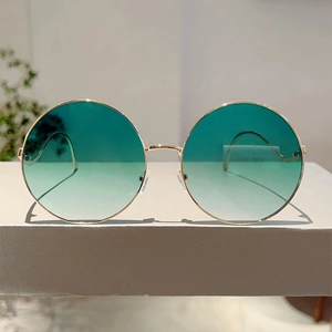 Detail of round gold metal frame sunglasses with gradient green lenses on display