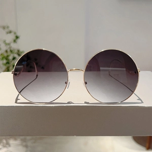 Close-up of golden round metal frame sunglasses with purple gradient lenses on stand
