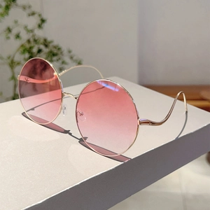 Detail of round sunglasses with pink gradient lenses and gold metal frame on desk