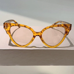 Detailed view of tortoiseshell cat-eye sunglasses with silver metal hinges on a light surface