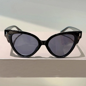 Detail of black cat eye sunglasses with silver rivets on a beige pedestal stand