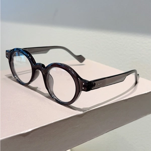 Detailed view of retro round frame glasses with metallic rivet accents on beige stand