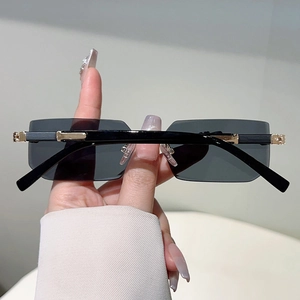 Detail of rectangular rimless sunglasses with wide black temples and gold metal accents