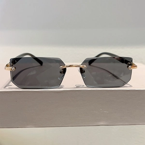 Close-up of rimless rectangular sunglasses with grey lenses and gold metal bridge detail
