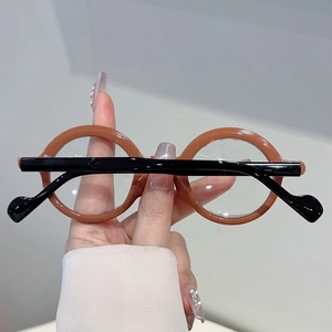 Detail view of round retro glasses with brown frame and black temples held by hand
