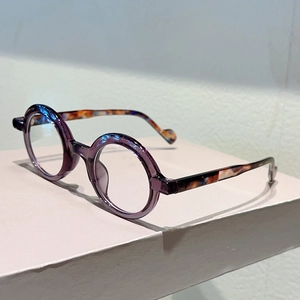 Detail view of round purple glasses frame with tortoiseshell temples on a stand