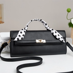 Detail of black pebbled leather handbag with gold twist lock and polka dot silk scarf handle