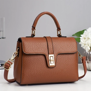 Detail of brown litchi texture leather handbag with golden rotating lock and top handle