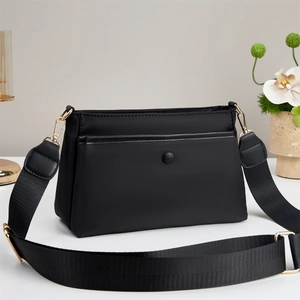 Close-up of black crossbody bag featuring golden hardware and adjustable woven strap