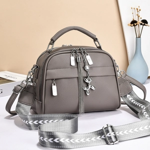 Detail of grey lychee textured crossbody bag with broad woven strap and silver puppy charm
