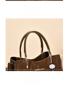 Close-up of brown textured leather tote with gold hardware and white floral charm detail