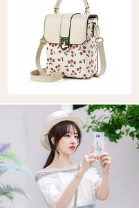 Close-up of a small beige bucket bag featuring a red and green cherry print with gold clasp