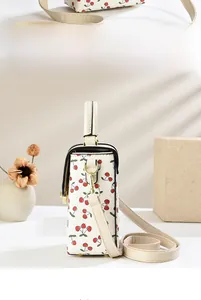 Detail view of cream white cherry print crossbody bag with metal lock and handle
