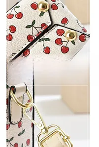 Detail view of cherry print bucket bag showing gold snap button and metal hook texture