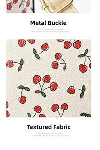 Detail of golden metal clasp and cherry print textured fabric on a mini crossbody bag