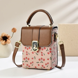 Mini brown leather crossbody bag with pink cherry print and golden clasp on beige background