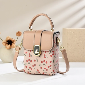Pink cherry print bucket bag with leather handle and golden lock in soft window sunlight