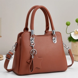 Brown lychee leather tote bag with silver chain star charm on white table surface
