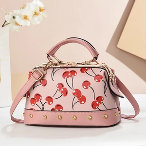 Detail of pink crossbody bag featuring red cherry prints and golden metal rivets at the base