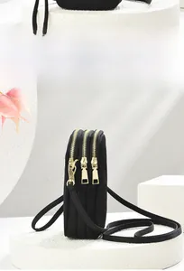 Detailed view of black multi-layer nylon crossbody bag with three gold zippers and long strap