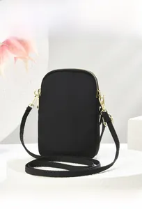 Detail view of the side and back of a black minimalist nylon crossbody phone bag with gold zippers
