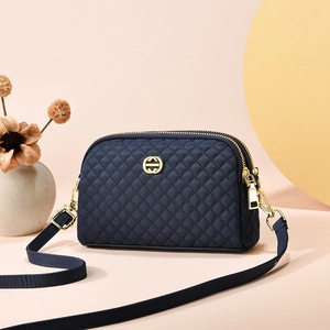 Sac bandoulière matelassé bleu marine avec détails dorés et double zip sur fond rose