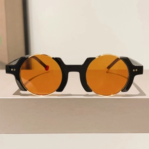 Detail of black irregular frames with orange lenses and gold studs on the temples