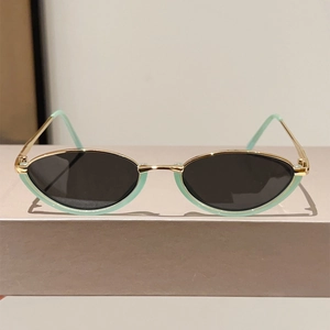 Detailed close-up of golden metal cat-eye sunglasses with mint green accents and dark lenses