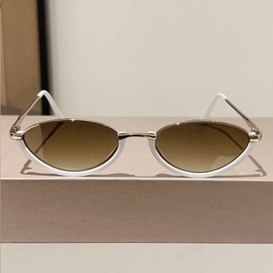 Detailed view of white and gold cat-eye sunglasses with tinted brown lenses on a stand