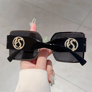 Detail of square black sunglasses featuring a bold gold circular logo on the temple arm