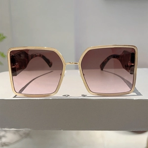 Detailed close-up of textured gold metal frames and gradient pink lenses on sunglasses
